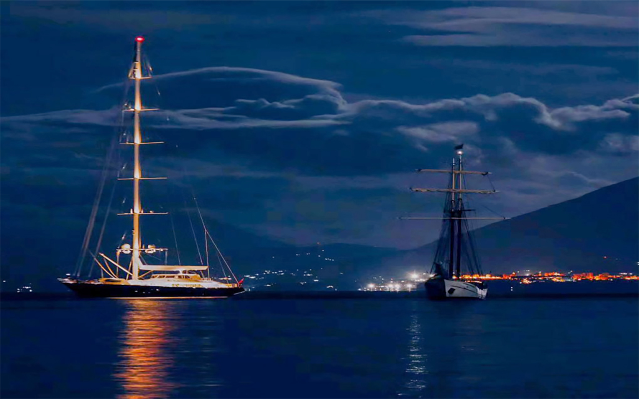 Hoàng hôn dần buông trên biển Địa Trung Hải lặng sóng khi siêu du thuyền Bayesian tiến gần đến thị trấn đánh cá nhỏ Porticello bên bờ biển phía bắc Sicily, Italy.